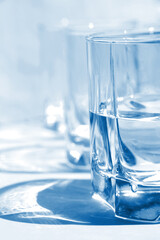 Sunshine through glass of water on background blue color, glare of glass, glass of water, glass of water