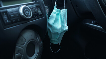 Surgical or medical mask is hanging beside the steering wheel of a car for going outside during covid19 pandemic, the concept of protection against bacteria and viruses