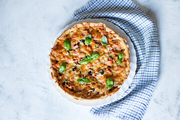 Delicious and crispy pizza with olives and sausages on a light background with a blue napkin, top view