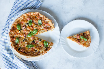 Delicious and crispy pizza with olives and sausages with a cut piece on a light background with a blue napkin, top view, copy space