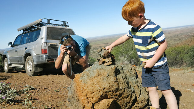 Father taking a photo of his young son making a rock tower in the outback