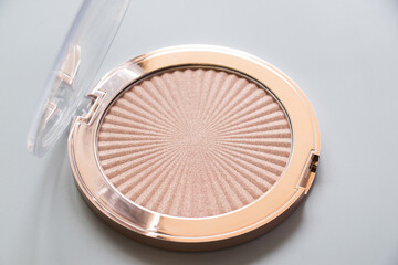 Highlighter, bronzer, cosmetic, makeup, gold, light. Highlighter for makeup on a grey background. Macro photography of highlighter for makeup on a grey background.
