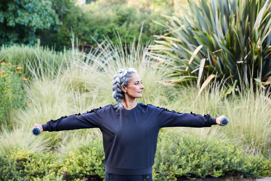 Mature woman with grey hair lifting weights and working out in backyard
