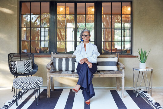 Portrait of beautiful and stylish mature woman interior designer with grey hair sitting on front porch