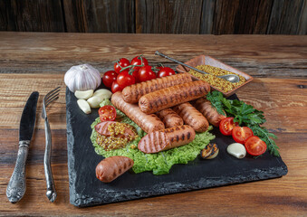 fried sausages, cherry tomatoes, garlic, dill, mustard sauce, knife, fork on a wooden table, rustic style, top view