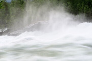 Obraz premium fast flowing flooded river current with violent waterfall