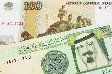 A macro image of a Russian one hundred ruble note paired up with a green and yellow on riyal bank note from Saudi Arabia.  Shot close up in macro.