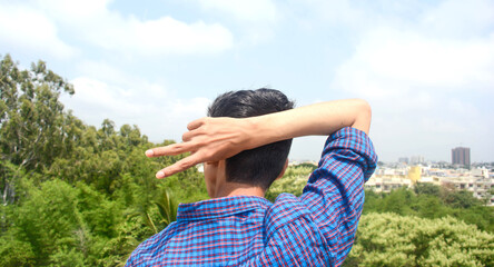 Back view of young man showing victory symbol. city background.