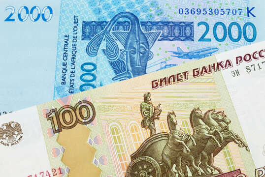 A macro image of a Russian one hundred ruble note paired up with a blue, two thousand West African franc bank note.  Shot close up in macro.