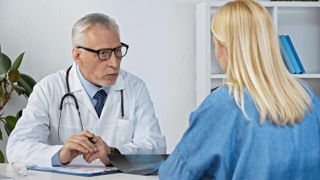 middle aged doctor talking with patient and looking at x-ray