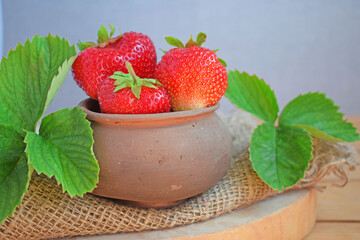 Fresh sweet strawberries in a clay pot on a wooden background.