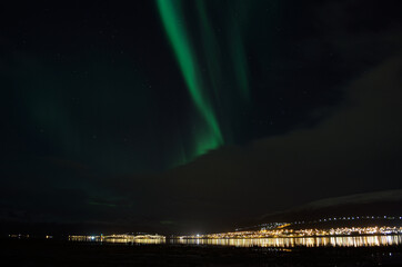 aurora borealis, northern lights over mountain landscape with new snow reflecting on beach sand and fjord water illuminated by the whale island settlement lights in late autumn