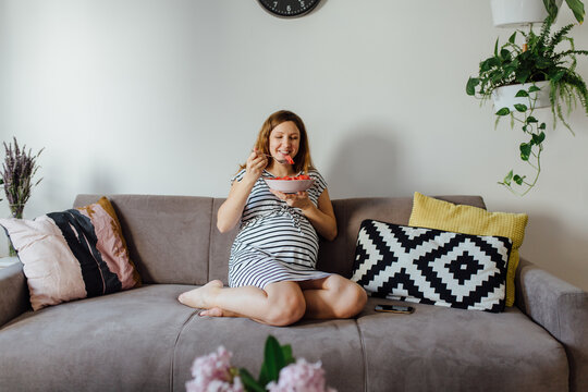 Pregnant woman eating watermelon on a cozy couch