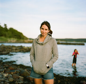 Mother standing on a rocky shore with a child in water behind her