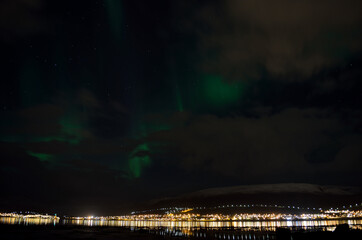 aurora borealis, northern lights over snowy mountain, reflective fjord water and whale island in northern norway in late autumn