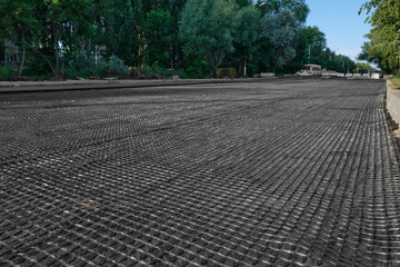 The construction of the road, laying of geomesh on soil before the asphalt pavement. Geogrid reinforcing a new roadbed, modern technologies.