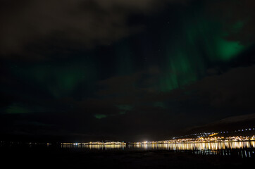 aurora borealis, northern lights over snowy mountain, reflective fjord water and whale island in northern norway in late autumn