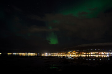Fototapeta premium aurora borealis, northern lights over snowy mountain, reflective fjord water and whale island in northern norway in late autumn