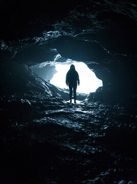 Silhouette of an explorer woman inside a cave next to the sea