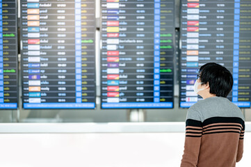 Asian man tourist wearing face mask holding suitcase luggage at arrival departure board in airport terminal. Coronavirus (COVID-19) pandemic prevention when travel. Social distancing concept