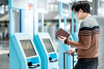 Fototapeta na wymiar Asian man tourist wearing face mask using self check-in kiosk in airport terminal. Coronavirus (COVID-19) pandemic prevention when travel abroad. Health awareness and social distancing concept
