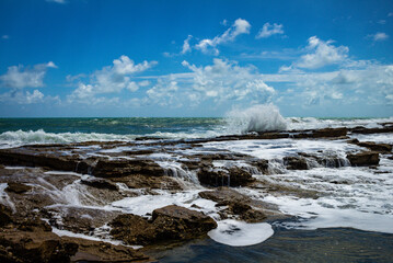 Coral reef at the edge of the sea bathed in sea foam. Small waterfalls of rocks below the horizon.