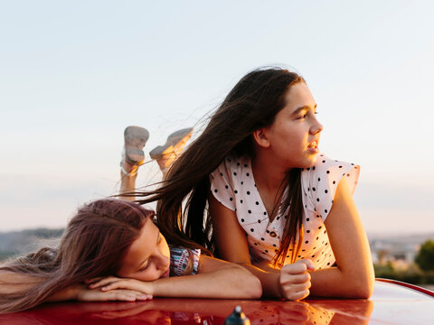 Teenage girls laughing at sunset on top of a red car.