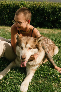 Short-haired girl with the malamut dog sit on the lawn at the park in the sun