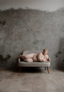 Front view of huge woman lying on gray sofa.