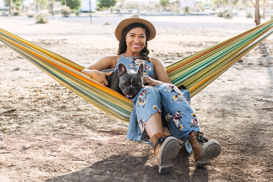 A woman sitting in a hammock with her french bulldog.