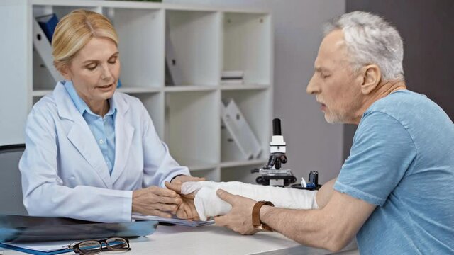 mature orthopedist touching arm cast of injured man