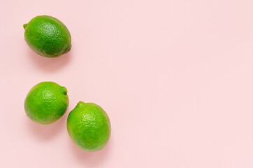 Three fresh juicy bright limes on a gentle pink light background with place for text. citrus vitamin C healthy eating. blank for postcards banner and menu