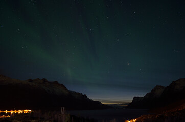 aurora borealis over mountain valley with fjord and settlement in the bottom