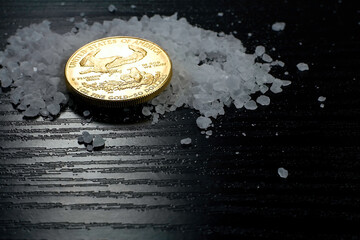 Concept: salt and gold. Gold coin American Eagle 1 ounce compared to salt as a value of life. Gold coin, coarse salt arranged on a table.