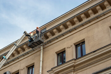 Obraz premium Reconstruction of the building of the Drama Theater in the city. Two working painters on an air platform paint a wall.