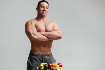 Sexy vegan guy with a naked torso posing in the Studio next to fruit. Diet. Healthy diet