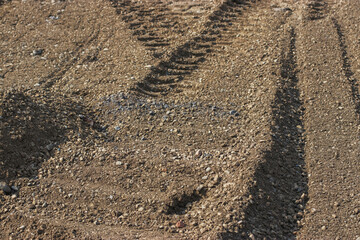 Traces of construction machinery wheels on sand and gravel. Road repair on a sunny summer day.