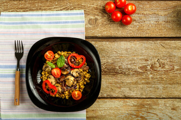 On a wooden table is a black plate of boiled mung bean with vegetables and mushrooms on a napkin and a fork. Copy space.