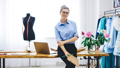 Portrait of attractive female owner of showroom planning event of fashion industry standing near...