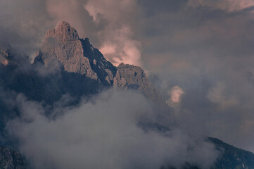 Dramatic view of mountain peaks wrapped in clouds at the golden hours of sunset in the Dolomites, South Tyrol, Italy.