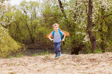 Preschool boy with wooden wings playing near river