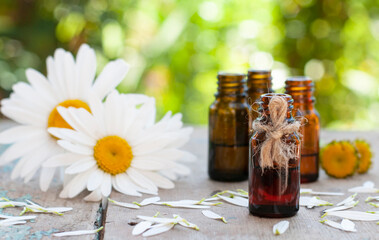 Essential oil in glass bottle with fresh chamomile flowers and leaves on the wood table top