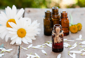 Essential oil in glass bottle with fresh chamomile flowers and leaves on the wood table top
