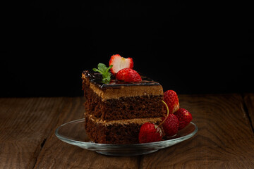 A slice of cake with strawberries on a glass plate against a dark background.