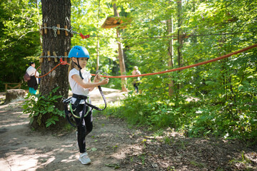 Naklejka na ściany i meble Rope adventure - a little girl with an insurance hook attached to the rope walking to the area