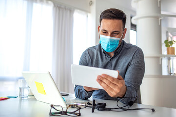 Fototapeta na wymiar Mature businessman with mask using digital tablet at work. Male employee wearing a health mask Preventing corona virus infection covid-19, concept of working from home and social distancing