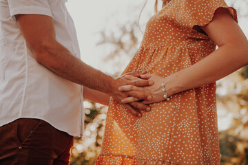 A pregnant woman and her husband and baby daddy-to-be holds hands on her stomach hugs his wife. Close-up of arms and abdomen. Pregnancy women