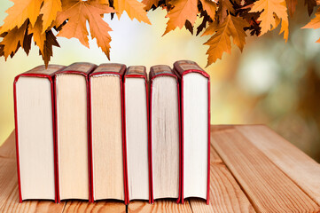 stack of books on the wood table with maple leaves on the autumn background