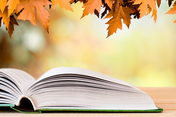 open book on the wood table on the autumn background with maple leaves