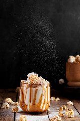 Milkshake with popcorn and caramel syrup on a black background. Sprinkle with powdered sugar.